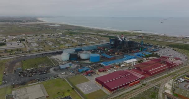 Images aériennes du site industriel au bord de la mer. Usine avec cheminées à rayures et salles de production près de l'autoroute côtière. Port Elisabeth, Afrique du Sud — Video