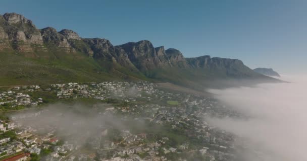Disparo descendente de escarpa rocosa por encima del destino turístico. Niebla saliendo del mar. Ciudad del Cabo, Sudáfrica — Vídeo de stock
