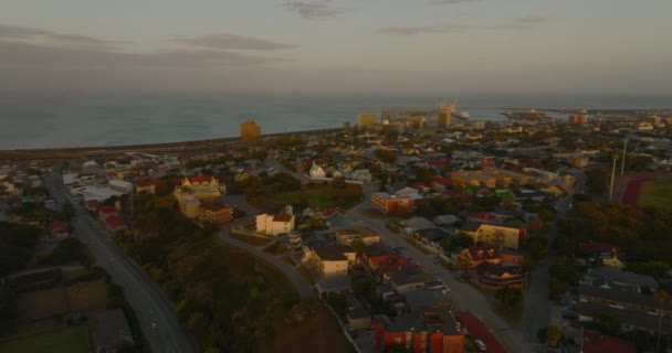 Deniz kıyısındaki konut binaları ve sanayi bölgesi güneş batarken aydınlatılıyor. Port Elisabeth, Güney Afrika — Stok video
