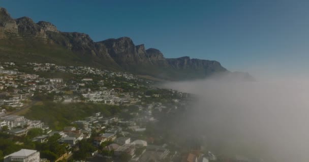 Вперед летят по туману, поднимаясь из моря вдоль берега. Жилые дома на склоне под скалистым откосом. Кейптаун, ЮАР — стоковое видео