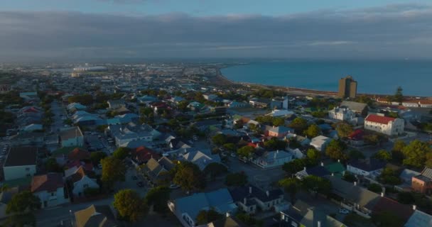 Luftaufnahme eines Wohnviertels in der Nähe der Küste, beleuchtet von untergehender Sonne. Meeresbucht im Hintergrund. Port Elisabeth, Südafrika — Stockvideo