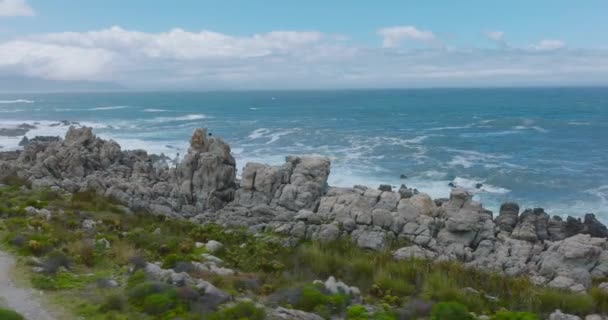 Grupo de turistas trepando por escarpadas rocas costeras. Orbita disparada alrededor de la gente viendo olas estrellarse en la costa. — Vídeos de Stock