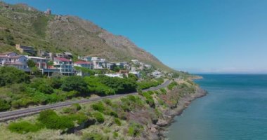 Tropikal deniz kıyısında uçun. Bisikletçi yolda bisiklete biniyor. Su yüzeyinin üstündeki yamaçta güzel evler..