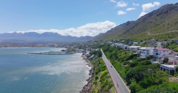 Vista aérea de la carretera costera que conduce a lo largo de la fila de casas de lujo. Vista panorámica de Gordons Bay con montañas en el fondo. — Vídeo de stock