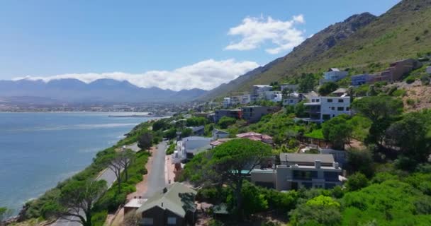 Día idílico y soleado en destino turístico. Bajo vuelo sobre casas en pendiente sobre el agua. Costa del mar y cresta de montaña en la distancia. — Vídeo de stock