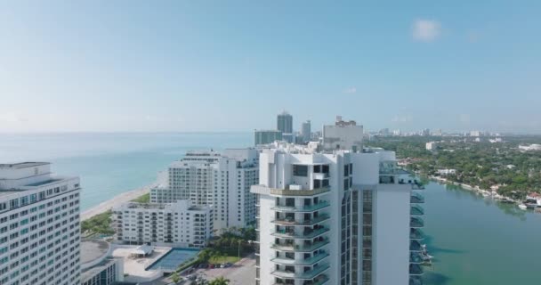 Adelante vuelan sobre la parte superior del edificio de apartamentos de gran altura en el moderno barrio urbano junto al mar. Día soleado en la ciudad. Miami, Estados Unidos — Vídeos de Stock