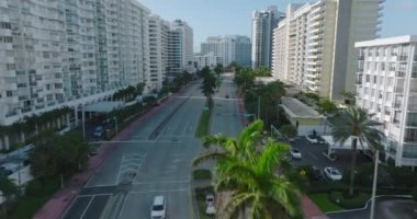 Modern kentsel ilçede çok şeritli ana yolda giden araçların takibi devam ediyor. Yol boyunca palmiye ağaçları. Miami, ABD