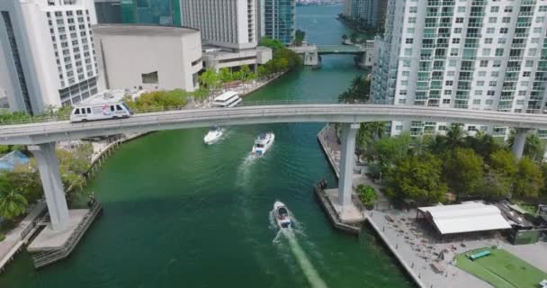Aerial descending footage of motorboats passing under Metromover rail car driving on high bridge. Futuristic city borough. Miami, USA — Stock videók