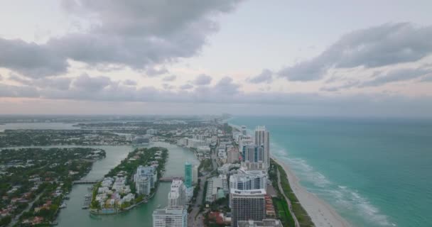 Aerial panoramic footage of modern urban borough on sea coast. Stripe of high rise buildings between sea and river at twilight. Miami, USA — Stock Video