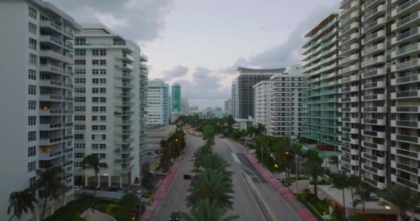 Multilane hoofdweg omzoomd door palmbomen passeren moderne stedelijke wijk. Voorwaarts vliegen langs flatgebouwen op meerdere verdiepingen in de schemering. Miami, Verenigde Staten — Stockvideo