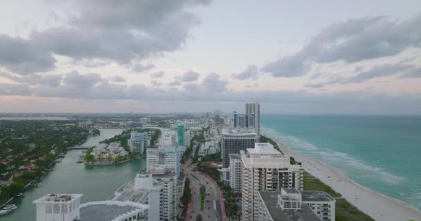 Посадочные кадры современного городского района на морском побережье в сумерках. Ряд роскошных многоэтажных жилых домов вдоль широкой дороги. Майами, США — стоковое видео