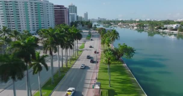 Tacking of cars driving on road on waterfront. Passing around yachts moored at bank. Multistorey apartment buildings in residential borough. Miami, USA — Vídeo de stock