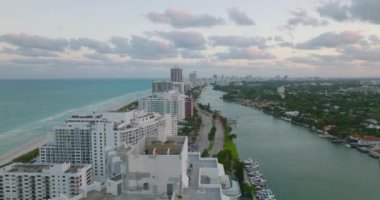 İleride deniz kıyısındaki çok katlı apartmanların ve limana giden çok şeritli yolların üzerinde uçuyoruz. Alacakaranlıkta hava manzarası. Miami, ABD