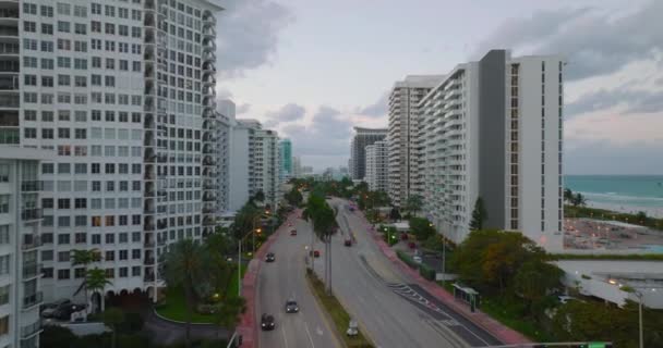 Tropikal bölgede rüzgarlı hava. Şehirdeki çok şeritli yol boyunca rüzgarda sallanan palmiye ağaçları. Günbatımında modern apartmanlar boyunca ileriye doğru uçar. Miami, ABD — Stok video