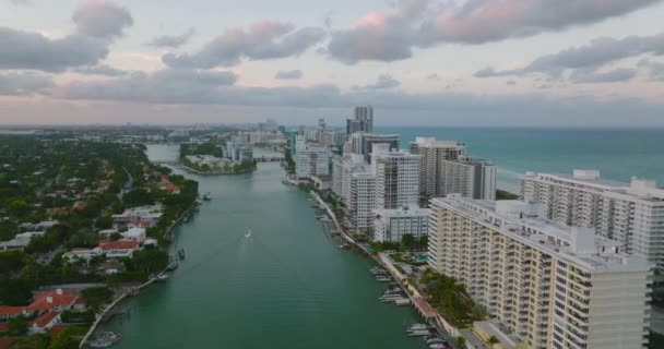 Widok z lotu ptaka na duże budynki mieszkalne wzdłuż wybrzeża o zachodzie słońca. Niski ruch na głównej drodze w mieście. Miami, USA — Wideo stockowe