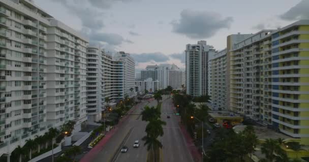 Avond in moderne stadsdeel met meerbaans hoofdweg omzoomd door hoge flatgebouwen. Voorwaarts vliegen in de schemering. Miami, Verenigde Staten — Stockvideo