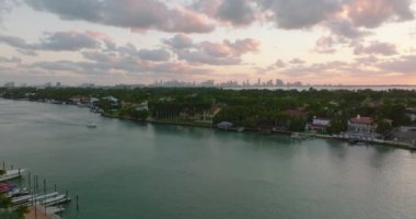 İleriye doğru su yüzeyinin ve yerleşim yerlerinin üzerinden uçun. Şehir merkezindeki gökdelenler renkli alacakaranlık gökyüzüne karşı. Miami, ABD