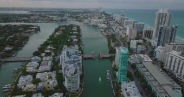 Yüksek açılı motorlu tekne kaldırılmış köprü altından geçiyor. Yoldaki kuyruklarda bekleyen araçlar. Şehir merkezinin üzerinden uç. Miami, ABD