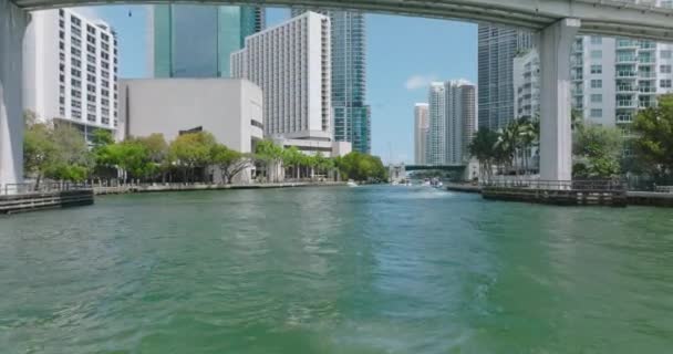 Forwards tracking of motorboat group passing under bridge in modern city. Miami river and downtown buildings on waterfronts. Miami, USA — Vídeos de Stock
