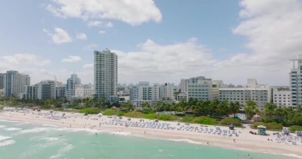 Forwards fly above beach on sea coast in tropical vacation resort. Revealing skyline with downtown skyscrapers. Miami, USA — Video
