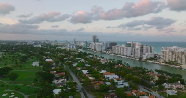 Voe acima do bairro residencial com casas baixas e vegetação verde rica. Listra de edifícios altos na costa do mar. Miami, EUA — Vídeo de Stock