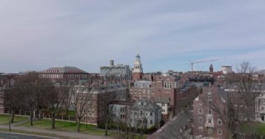 Harvard Üniversitesi kompleksindeki kırmızı tuğlalı binaların ilkbahar çekimi. İleriye doğru uçar ve yapraksız ağaçlar sıralanır. Boston, ABD