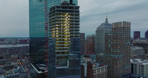 Beleuchtete Baustelle eines modernen Hochhauses in der Nähe des John Hancock Tower. Erhöhte Dia- und Schwenkaufnahmen in der Abenddämmerung. Boston, USA — Stockvideo