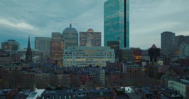 Alacakaranlıkta ışıklı pencereleri olan şehir merkezindeki büyük ofis binaları. İleri, şehrin üzerinde uçar. Boston, ABD