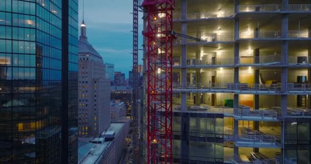 Красная фермовая конструкция башенного крана закреплена на строящемся высотном здании. В центре города в сумерках. Бостон, США — стоковое видео