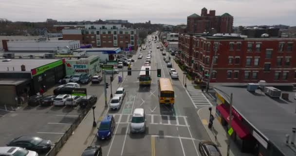 Forwards tracking of yellow school bus in streets of urban neighbourhood. Buildings with red brick facades. Boston, USA — Vídeo de stock