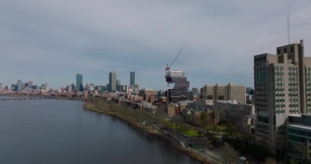 Forwards fly along waterfront. Construction of modern university building. Downtown skyscrapers in background. Boston, USA — Vídeo de stock