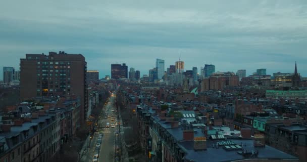 Za soumraku leťte nad řadami činžovních domů z červených cihel v obytné městské čtvrti. Vysoký kopec v centru budovy v pozadí. Boston, USA — Stock video