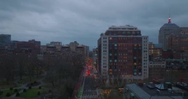 Akşam kentinde işlek caddenin üzerinden geriye doğru uç. Şehir merkezinde binalar ve alacakaranlıkta parklar. Boston, ABD