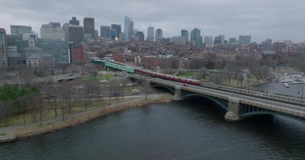 Letecké záběry jednotky metra přecházející řeku přes most a zastavující ve stanici. Cityscape na zamračený den v pozadí. Boston, USA — Stock video