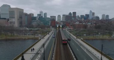 Tren biriminin istasyona gelişini takip ediyoruz. Yollarla çevrili metro rayları. Arka planda şehir binaları olan şehir manzarası. Boston, ABD
