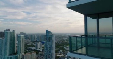 Balkonlu, modern, yüksek katlı bir apartmanın etrafında uçmak. Gün batımına karşı şehrin hava panoramik manzarası. Miami, ABD