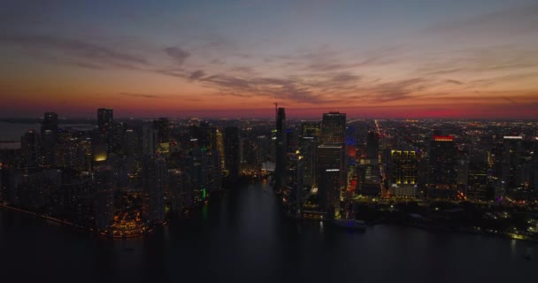 Moderní výškový mrakodrap v centru města na nábřeží proti romantické barevné obloze. Letecký panoramatický večerní snímek. Miami, USA — Stock video