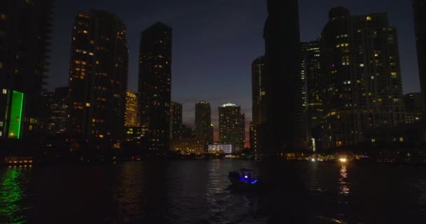 Low forwards fly above water surface between silhouettes on high rise downtown buildings on banks. Night city scene. Miami, USA — Stock Video