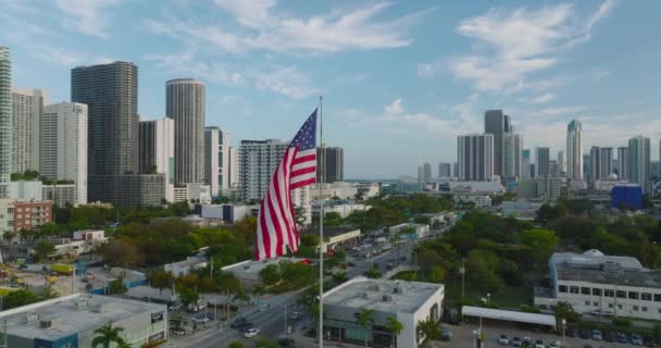 Şehrin üzerinde bayrak sallayarak Amerikan bayrağını dalgalandırın. Yüksek katlı ofis ya da arka plandaki apartmanlar. Miami, ABD — Stok video