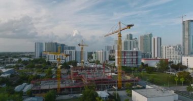 Alacakaranlıktaki inşaat alanındaki vinçlerin kayma ve pan görüntüleri, arka plandaki kentsel gelişim. Miami, ABD