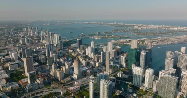 Amazing aerial footage of modern high rise buildings in city lit by late afternoon sun. Sea bay with islands in background. Miami, USA — Stock Video