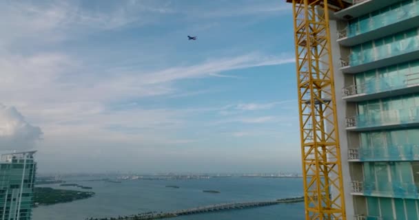Tył ujawnia plac budowy nowoczesnego wieżowca na nabrzeżu. Samolot przelatujący przez nagrania. Miami, USA — Wideo stockowe