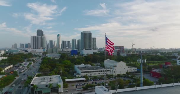 Étoiles et rayures ondulant dans le vent à l'heure d'or. Orbite autour du drapeau américain avec la ville moderne en arrière-plan. Miami, États-Unis — Video