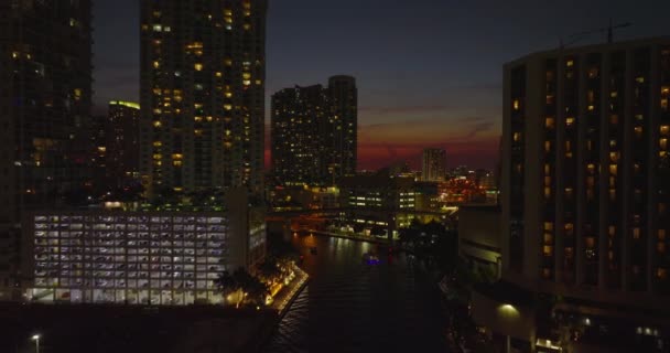 Backwards fly above river in city. Revealing bridge with road traffic. Evening view against twilight sky. Miami, USA — Stock Video