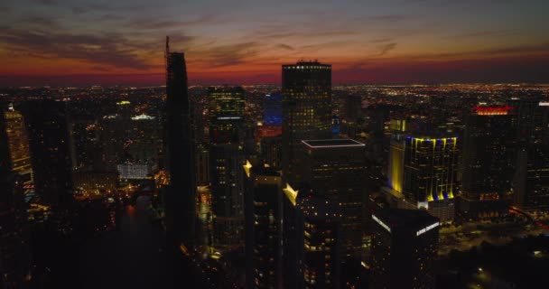 Tiro aéreo da noite de edifícios altos do centro da cidade contra o céu colorido após o pôr do sol. Desenvolvimento da cidade iluminado. Miami, EUA — Vídeo de Stock