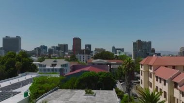 Şehir merkezindeki binalar ve ağaçlar üzerinde alçak uçuş. Açık mavi gökyüzüne karşı çok katlı ofis ya da apartman evleri. Cape Town, Güney Afrika.