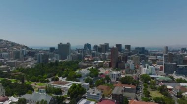 Şehir parklarında çeşitli binalar ve ağaçlar var. Arka planda yüksek binalar ve deniz olan şehir manzarası. Cape Town, Güney Afrika.