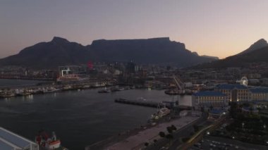 Kasabadaki deniz kıyısının tersten görünümü. Marina ve rıhtımdaki binalar, Masa Dağı 'nın silueti renkli alacakaranlık gökyüzüne karşı. Cape Town, Güney Afrika.