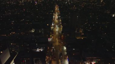 Gece şehrinin yüksek açılı manzarası. İleri doğru, çok şeritli caddelerde ilerleyen araçların üzerinden uçar ve karanlığa doğru parlarlar. Manhattan, New York City, ABD.
