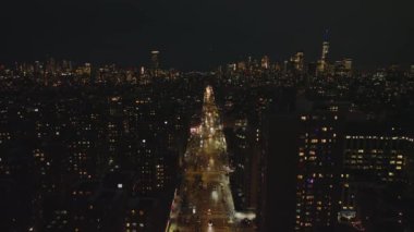 Aydınlatılmış caddenin ve gece etrafındaki binaların hava panoramik görüntüleri. Şehir merkezinde gökdelenler var. Manhattan, New York City, ABD.